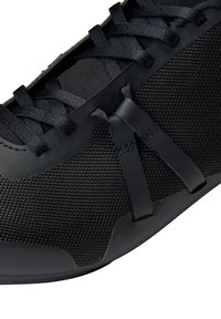 Scarpa sportiva nera con tomaia in rete testurizzata, lacci piatti e suola in gomma liscia. Include dettagli eleganti per un rinforzo.
