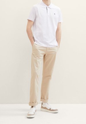 Polo blanc à manches courtes, chinos beiges et baskets blanches avec des accents beiges. Comprend un col et un petit logo de la marque sur le polo.