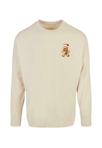 Cremefarvet sweatshirt lavet af blødt stof, med et lille ingefærbrød karakter iført en julesok på venstre bryst.