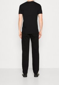 Schwarzes T-Shirt mit kurzen Ärmeln, von hinten gesehen, aus weichem Material. Kombiniert mit schwarzen, geraden Hosen und schwarzen Schuhen. Minimalistisches Design.