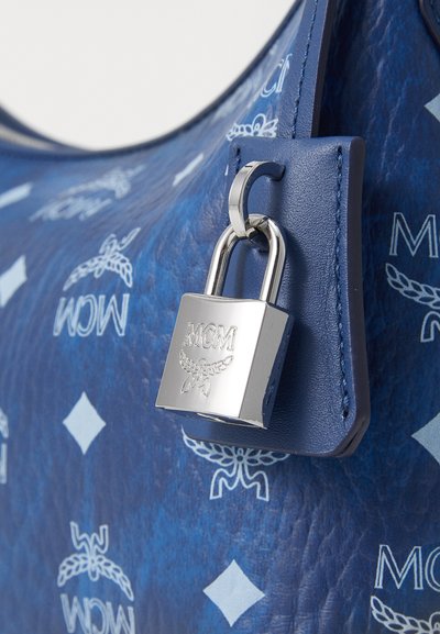 Sac à main en cuir bleu avec un motif embossé et une quincaillerie à cadenas en argent. Texture lisse avec le logo MCM en bleu clair.