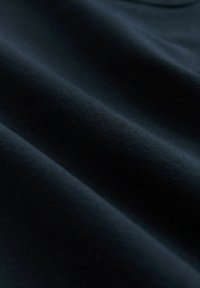Tessuto nero con texture liscia e opaca, caratterizzato da leggere pieghe e dettagli di tessitura fine. Nessun motivo o accessorio visibile.