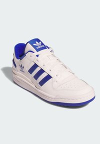 Biele nízke tenisky Adidas s modrými pruhmi, modrou vnútornou podšívkou a logom Adidas na jazyku a strane, zobrazené mierne z uhla.