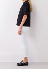 Svart T-shirt med kort ärm och bröstficka, tillsammans med vita avkortade jeans och svarta lackskor. Minimalistisk design, avslappnad outfit.