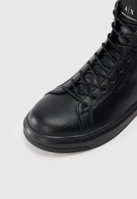 Zapatilla alta negra hecha de cuero texturizado, con punta redondeada, diseño de cordones y suela de goma sólida con un sutil estampado.