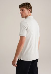 Polo majica s kratkimi rokavi iz svetlo bež tkanine, s klasičnim ovratnikom, stranskimi razporki in gladko teksturo. Primerna za casual oblačenje.