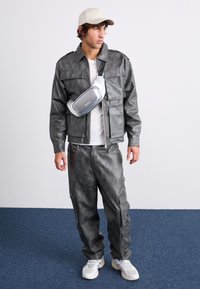 Veste et pantalon en simili cuir gris avec une texture lisse, associés à une casquette légère et un sac banane argenté. Des baskets complètent la tenue.