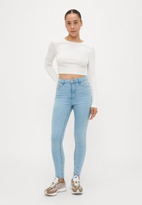 Lyseblå skinny jeans med høy midje, kombinert med en kortermet hvit skjorte. Outfitten kompletteres av grå og hvite joggesko.