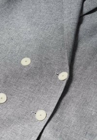 Gros plan sur un tissu gris à fine armure diagonale avec quatre boutons blancs cousus en deux rangées verticales parallèles.