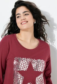 Bordeaux lange mouwen t-shirt van zachte stof, met een zilveren sterafbeelding en een textuurpatroon van schubben over de voorkant.