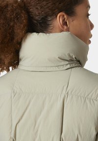 Giacca a vento beige chiaro con colletto alto, texture trapuntata e cuciture visibili lungo le cuciture. Materiale sintetico morbido.