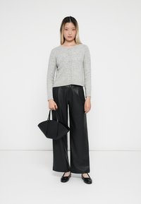 Cardigan en laine gris tricoté avec des boutons, associé à un pantalon large en cuir noir et des chaussures plates noires. Tenant un petit sac noir.