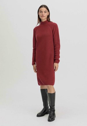 Robe en tricot rouge avec un col montant, texture côtelée, manches longues et coupe décontractée, associée à des bottes noires jusqu'aux genoux.