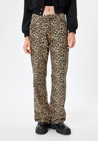 Leopard print wide-leg pants in beige and black with an elastic waistband. Textured fabric with a mix of animal patterns. Black chunky shoes.