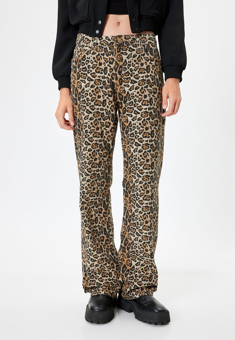 Haremshose mit Leopardenmuster in Beige und Schwarz, ausgestattet mit einem elastischen Bund. Texturiertes Material mit einer Mischung aus Tiermustern. Schwarze klobige Schuhe.