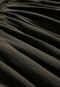 Tissu sombre avec des plis doux et profonds créant des crêtes parallèles lisses et des ombres, mettant en valeur la texture et la chute.