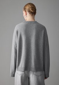 Grau Wollpullover mit geripptem Ausschnitt und Bündchen, mit lockerer Passform und überschnittenen Schultern. Strukturiertes, weiches Finish, kombiniert mit hellgrauen Jeans.