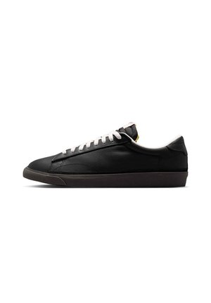 Sort lav top sneaker med hvide snørebånd og en mørk sål, vist fra siden på en hvid baggrund.