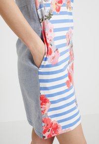 Floral-patterned dress featuring blue and white stripes, with a denim-like side panel and pockets on each side. Bright, textured fabric.