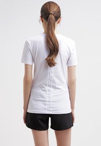 Vit t-shirt med kort ärm och rak skärning, med en central sömdetalj på baksidan. Matchad med svarta shorts.