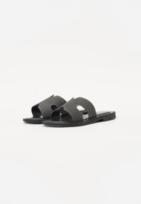 Sorte strandsandaler med en teksturert stoffoverdel, som har to kryssede stropper og åpen tå-design; flat gummisål.