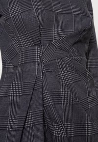 Robe noire et grise à motif en tissu texturé tissé, avec un design à carreaux et un détail drapé sur le côté.