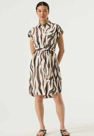 Robe chemise boutonnée couleur crème avec des rayures zèbre noires et marron. Manches courtes, taille ceinturée et une seule poche poitrine. Texture de tissu lisse.