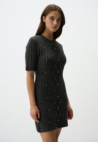 Robe tricotée grise à manches courtes avec une texture côtelée, présentant des motifs en diamant et de petites perles décoratives le long de l'avant.