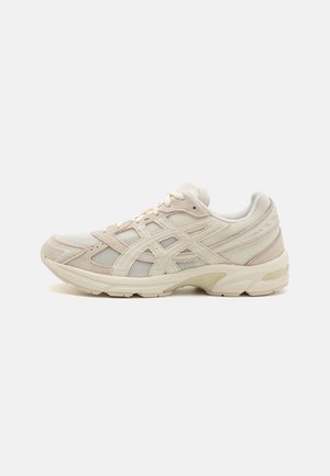 Beżowy i kremowy sportowy sneaker z siateczkową i zamszową cholewką, grubą amortyzowaną podeszwą oraz wzorzystymi bocznymi paskami, pokazany od zewnętrznej strony.