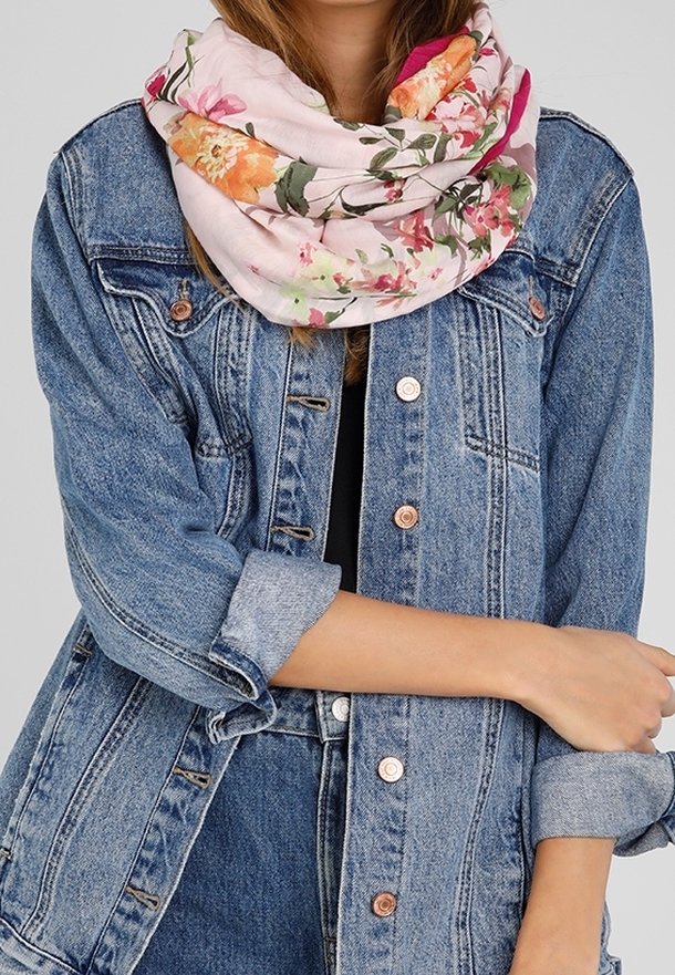 Femme portant une écharpe rose à fleurs et une veste en jean bleue aux manches retroussées avec un pantalon en jean assorti, bras croisés.