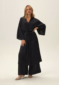 Black satin kimono robe featuring wide sleeves, a belt, and a smooth texture, paired with wide-leg black pants and strappy silver heels.