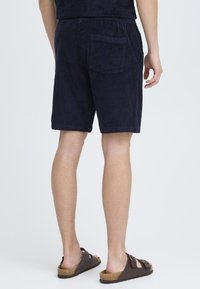 Mørkeblå corduroy-shorts med elastisk liv, sidetasker og bakfick, samt en teksturert finish, kombinert med brune sandaler.