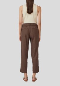 Un pantalon marron ample avec une taille élastique, deux poches arrière et une coupe décontractée, associé à un débardeur crème.
