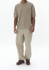 Béžový pletený top s krátkým rukávem v kombinaci s volnými kalhotami světle béžové barvy a hnědými šněrovacími botami, s jemnou texturou a tkanými detaily.