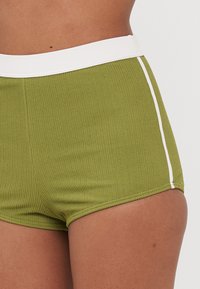 Olivengrønne ribbestrikkede shorts med hvit elastisk midjebånd og siden accent. Har en tettsittende fasong og glatt tekstur.