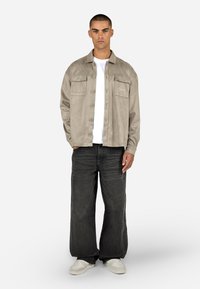 Beige szarusahátéj pólódzseki két elülső zsebbel, gombos záródással és hímezett részletekkel. Laza fekete farmerral és fehér sportcipőkkel párosítva.