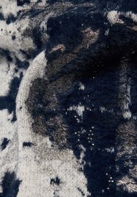 Weiche Strickware mit einem marineblauen und silbernen Muster sowie kleinen metallischen Akzenten, die eine weiche Textur mit visueller Tiefe verbinden.