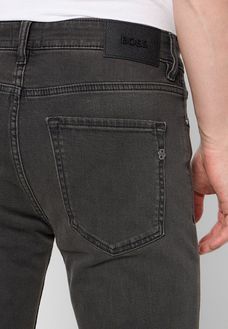 Jeans in denim grigio scuro con tasca posteriore standard e una patch in pelle nera con logo impresso sulla cintura.