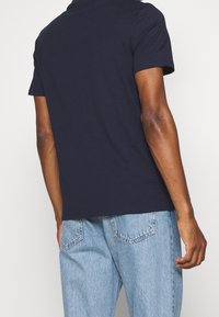 T-shirt a maniche corte blu navy in cotone, con scollatura rotonda e vestibilità ampia, abbinato a jeans in denim azzurri.