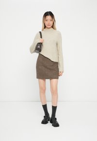 Vaaleanbeige neulottu villapaita korkealla kaula-aukolla, yhdistettynä ruskeaan houndstooth-hameeseen. Asusteina pieni tumman laukku ja mustat kengät.