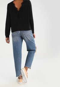 Maglietta nera a maniche lunghe con scollatura a V rifinita in pizzo, abbinata a jeans chiari strappati e sneakers beige.