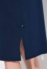 Tmavě modré bavlněné šaty s bočním rozparkem na spodním lemu a malou značkovou nášivkou blízko švu. Hladká textura a jednoduchý design.