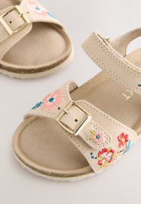 Beige sandalen met bloemrijke borduursels in roze, rood en blauw, voorzien van een gespsluiting en een gestructureerd voetbed. Rubberzool voor grip.