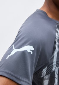 Halli sportliku särke varrukas, millel on valge Puma logo hüppavast kassist ülaosas.