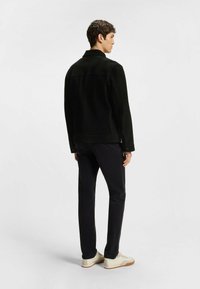 Svart mockajacka med krage och knäppning framtill, matchad med åtsittande svarta byxor och ljusa sneakers. Enkel design, utan mönster.