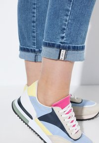 Baskets multicolores présentant des panneaux bleus, roses, jaunes et beiges. Lacets blancs, tissu doux et semelle en caoutchouc texturée. Manches en denim retroussées au-dessus.