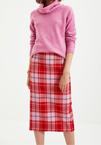 Rosa cowl-neck tröja och röd rutigt midikjol med rosa, röd och svarta detaljer, som har en mjuk textur och en figurnära silhuett.