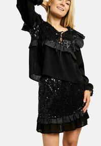 Črna obleka z bleščicami s krakastimi rokavi in krilom, ki ima teksturiran panel in zavezovanje na vratu. Mehka tkanina s sijočimi poudarki.