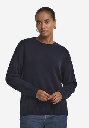 Marinblå stickad tröja med rund halsringning, ribbade ärmslut och nederkant. Har en avslappnad passform och mjuk textur. Bärs ihop med blå jeans.