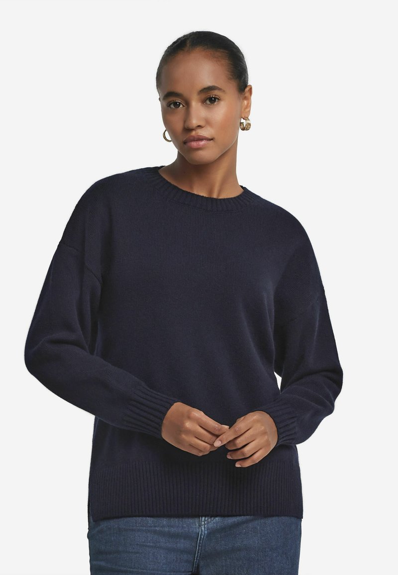 Marineblauer Strickpullover mit Rundhalsausschnitt, gerippten Bündchen und Saum. Hat eine lockere Passform und weiche Textur. Getragen mit blauen Jeans.